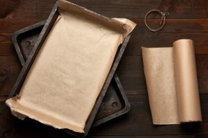 empty rectangular metal pan covered with brown parchment paper and paper rolls on a wooden table, top view